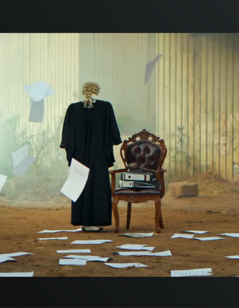 Photo: Person in a dark robe walks past scattered papers toward an ornate burgundy chair in a hall.