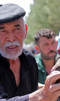 Man in dark jacket reaches toward a woman wearing a colorful headscarf and backpack outdoors.