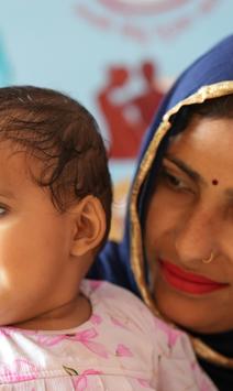 Mother in blue headscarf with a gold band cradles a smiling baby in pink.