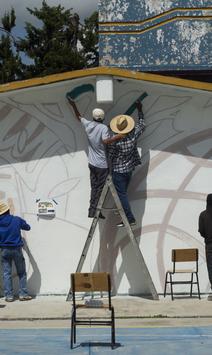 Outdoor stage under a white tent; central performer in gray raises arms, flanked by crew.