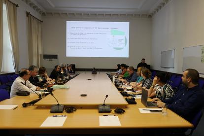 A conference room with participants seated around a long table, a presentation on the screen.