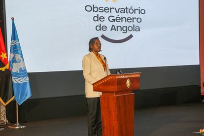 A speaker stands at a podium in front of a screen displaying the "Observatório de Gênero de Angola" logo.