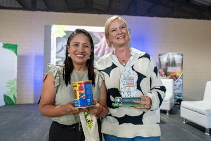Two women smiling while holding awards and gifts at an event, colorful background.