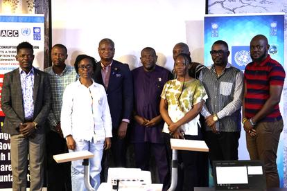 Group of nine individuals posing together, smiling at an indoor event with banners in the background.