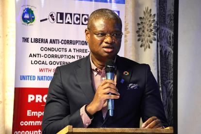 A man speaks into a microphone at a podium, with a banner in the background.