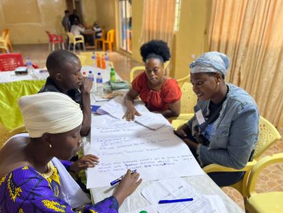 A group of four people collaborate around a table covered with papers and pens.