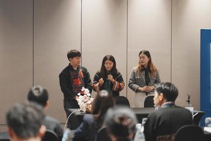 Three speakers present at a conference with an audience seated in front.