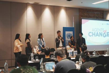 Six individuals stand on stage, engaging with an audience in a conference setting.