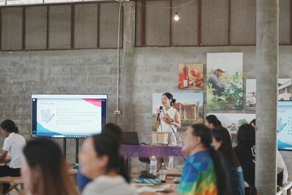 A presenter speaks in front of a group in a bright, industrial space with screens.