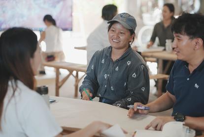 Three people engaged in a discussion around a table in a bright, casual setting.