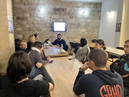 Group of people engaged in a discussion around a table in a well-lit room.