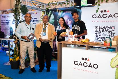 Five people at a cacao booth pose for a photo at a trade show, with signage and products.