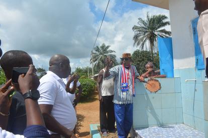 Outdoor scene with people near a blue wall; palm trees, a man in striped shirt speaking.