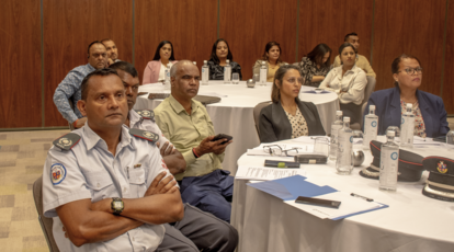 Group of diverse adults seated around a conference table in a wood-paneled room.
