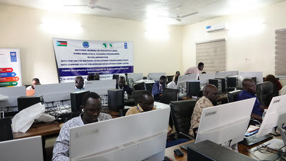 Classroom computer lab with many students at desks and a banner at the back.