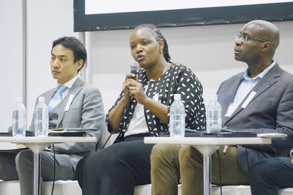 Photograph of three panelists seated at a table; middle panelist speaks into a microphone.
