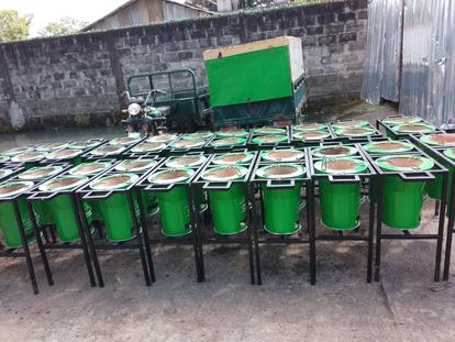 Row of green plastic drums with white lids on metal frames outdoors.