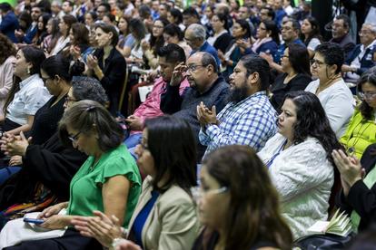 Crowded audience seated at an event, diverse attendees watching attentively.