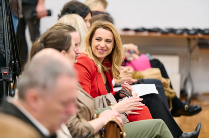 Audience seated in a conference hall, some taking notes.