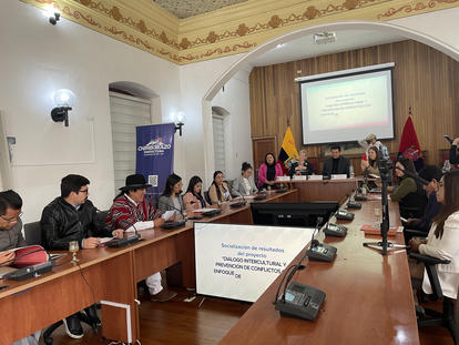 Formal conference with people around a long table and a projection screen at the front.
