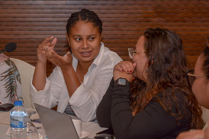Photograph of three people at a table in discussion, laptop and water bottle visible.