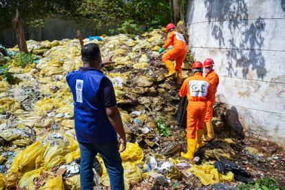 Blue-shirted man with number 7 watches orange-clad workers inspect muddy rubble by a concrete wall.