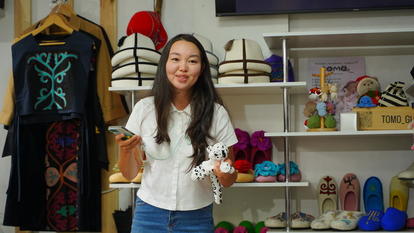 Woman wearing white top and jeans stands in a colorful boutique with hats and shoes.