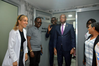 Five people in business and casual outfits stand in a bright hallway, smiling at the camera.