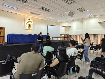 Audience seated in a conference room facing a stage with a projector screen.