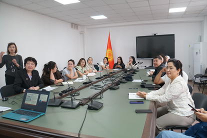 Professionals in a conference room around a long table with laptops; red flag with yellow stars.