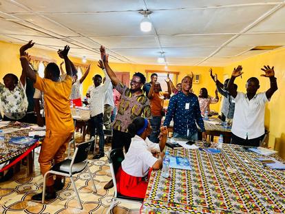People with raised hands in a bright room with yellow walls and patterned tables.