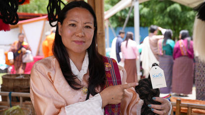 Blurred person in peach outfit being interviewed at a street market; microphone with logo in frame.