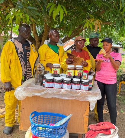Group of people in colorful clothes around a table with jars of goods outdoors.
