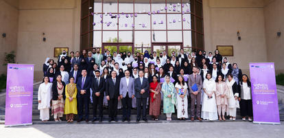 Large group of people in formal attire posing on building steps beside purple banners.