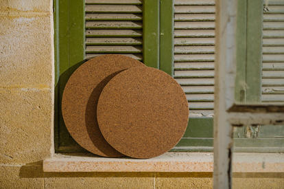 Two circular cork coasters resting on a stone windowsill under green shutters.