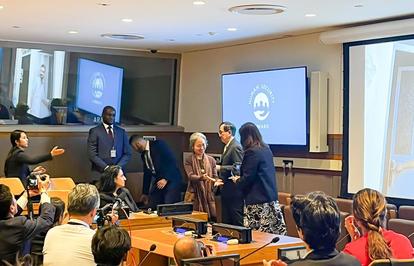 Conference room: presenters at the front, audience seated; projector displays a circular logo.