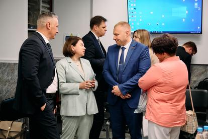 Group of professionals in suits and smart casual outfits converse in a conference room.