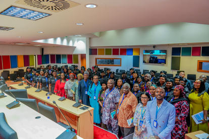 Large group of people with lanyards posing for a group photo in a colorful conference room.