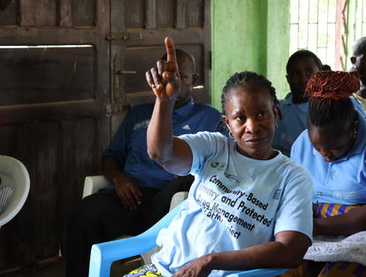 Photo: woman in a light blue shirt raises her hand in a classroom-like room; others sit.