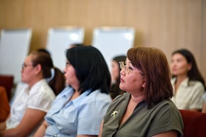 Audience of adults seated in a conference room, listening attentively.