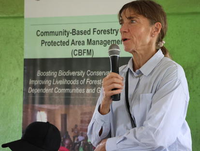 Photograph of a man in a light blue shirt speaking into a handheld microphone at a forestry event.