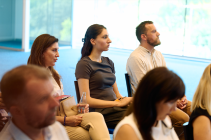 Group of people seated in a bright conference room, attending a meeting.