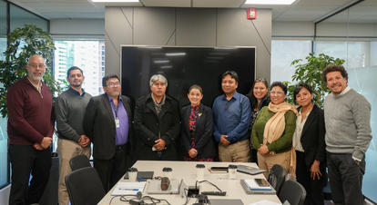 Group photograph of professionals posing in a modern office conference room with laptops.