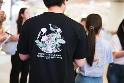Back view of a person in a black t-shirt with a white graphic, in a crowded indoor setting.