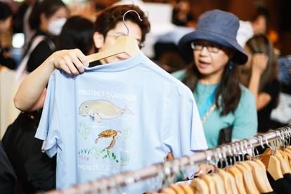 Photo: shopper holds up a light-blue shirt with a fish graphic in a busy clothing store.