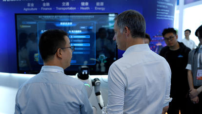 Photograph: two men at a tech expo booth, blue screens and devices in the background.