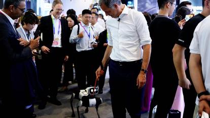 Photograph of professionals in suits surrounding a small robot on a table at a conference.