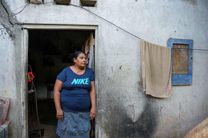 Man in a blue Nike T-shirt stands in a doorway of a weathered gray building; towel on the window.