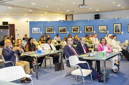 Audience seated at tables in a blue-walled conference room watching a presentation.
