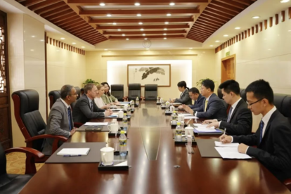 Photo of suited professionals around a long wooden conference table in a wood-paneled room.